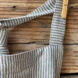 Gaiši zilas/dabīgi pelēkas svītriņas (~2.5mm), viegli mīkstināta lina auduma priekšauts ar kabatiņu un regulējamām lencēm