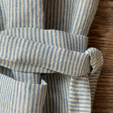 Gaiši zilas/dabīgi pelēkas svītriņas (~2.5mm), viegli mīkstināta lina auduma priekšauts ar kabatiņu un regulējamām lencēm