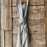 Gaiši zilas/dabīgi pelēkas svītriņas (~2.5mm), viegli mīkstināta lina auduma priekšauts ar kabatiņu un regulējamām lencēm