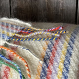 Krāsainas svītriņas uz piena balta fona aitas vilnas pleds ar bārkstīm