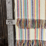 Krāsainas svītriņas uz piena balta fona aitas vilnas pleds ar bārkstīm